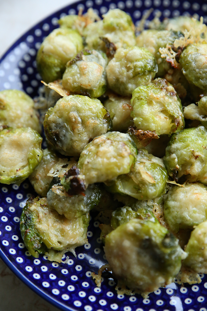 A large dark blue with white polka dots round platter with smashed parmesan Brussel sprouts.