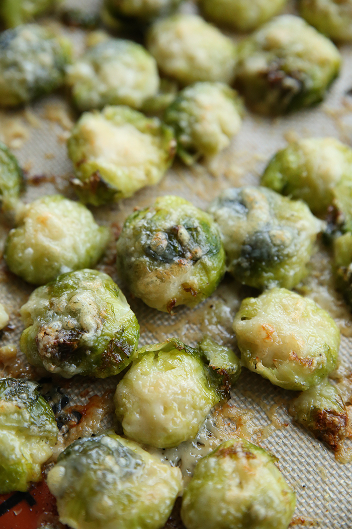 Smashed parmesan brussels sprouts on a large baking sheet with a silicone baking mat on the bottom.