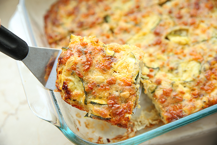 Zucchini pizza casserole in a glass 9x13 baking dish with a piece cut out of a corner held above with a serving spatula.