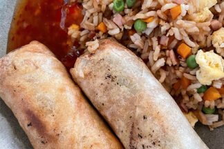 Two egg rolls, sweet chili sauce, and a serving of fried rice on a plate.
