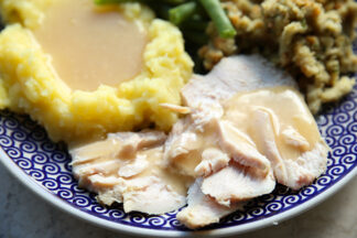 A dark blue plate with a swirled pattern with a serving of turkey breast topped with gravy, a serving of mashed potatoes and gravy and stuffing.