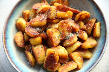 A serving bowl full of super crispy roasted potato chunks tossed with Parmesan cheese and parsley flakes.