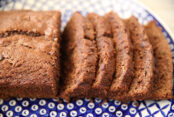 A loaf of chocolate zucchini bread partially sliced sitting on a dark blue Polish pottery plate with a bubble white pattern and a lattice pattern around the edge.