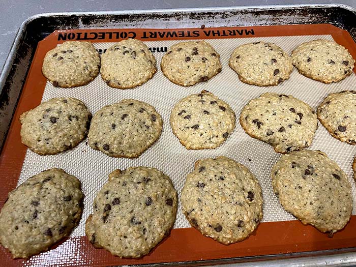 A cookie sheet lined with a silicone baking mat filled with baked banana oatmeal cookies with chocolate chips.