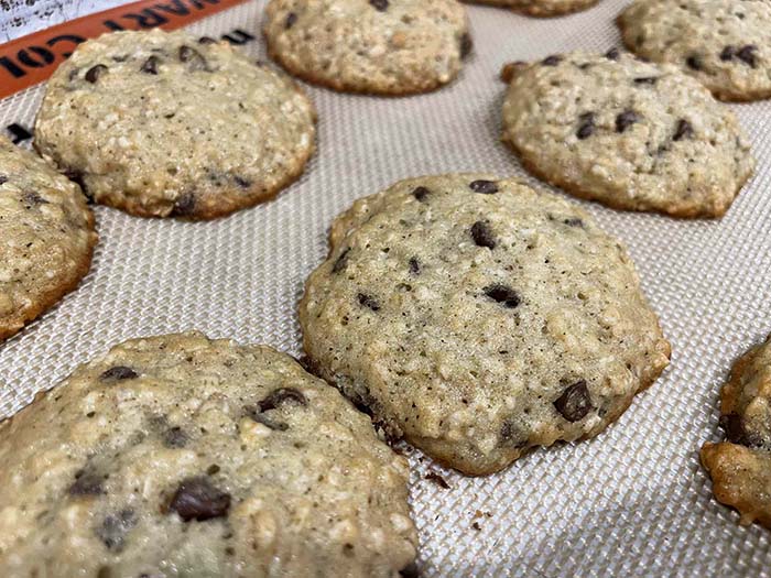 Several banana oatmeal chocolate chip cookies on a cookie sheet lined with a silicone baking mat.