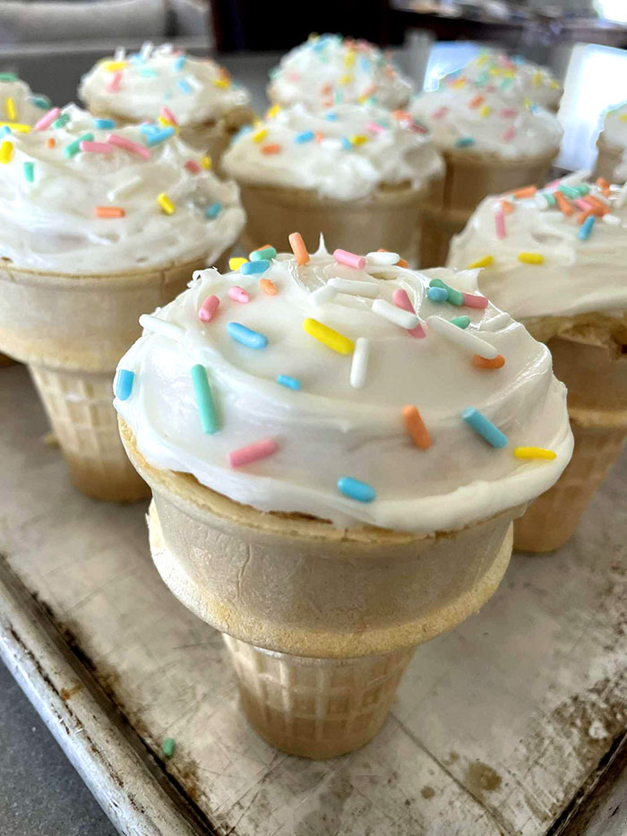 A baking sheet filled with ice cream cone cupcakes with vanilla frosting and sprinkles.