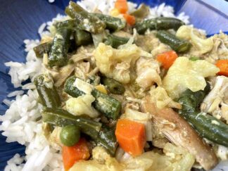 Shredded chicken curry with green beans, diced carrots, corn, and peas served over white rice on a dark blue plate.