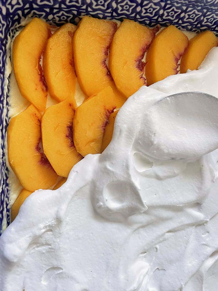 A 9x13 baking dish with a layer of sliced peaches in a corner and Cool whip covering the rest.