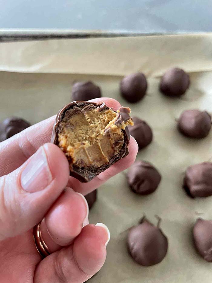 Healthy peanut butter balls on a parchment-lined baking sheet with a bitten-in-half healthy peanut butter held above the baking sheet.