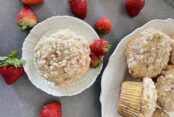 A strawberry rhubarb muffin on a small plate with two whole strawberries on the left. A partial picture of a plate bowl with strawberry rhubarb muffins. Whole strawberries are scattered around the small plate.