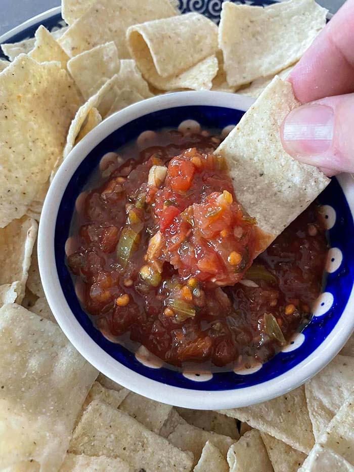 A bowl of homemade salsa on a large round plate with tortillas surrounding the bowl.