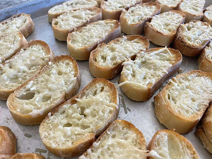 A sheet pan full of toasted parmesan baguette slices.