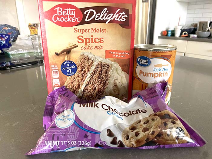 A spice cake mix, a can of pumpkin, and a bag of milk chocolate chips sitting on a counter.