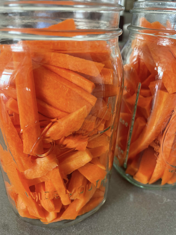 Two glass canning jars without lids filled with carrot sticks.