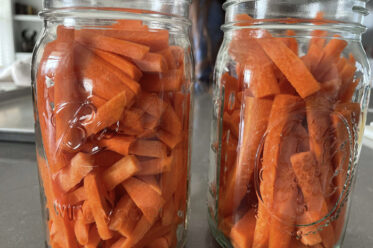 Two glass canning jars filled with carrot sticks. The jars are without lids