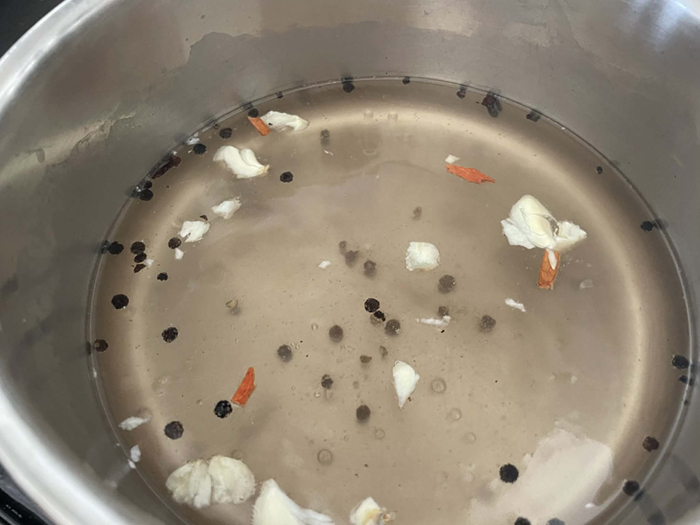 A saucepan with white vinegar, water, sugar, smashed garlic clove, salt, and black peppercorns.