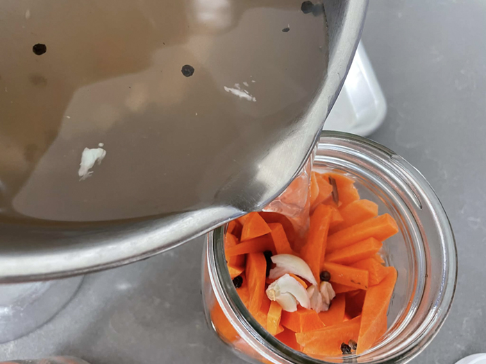 A brine mixture in a saucepan being poured into a jar of carrot sticks.