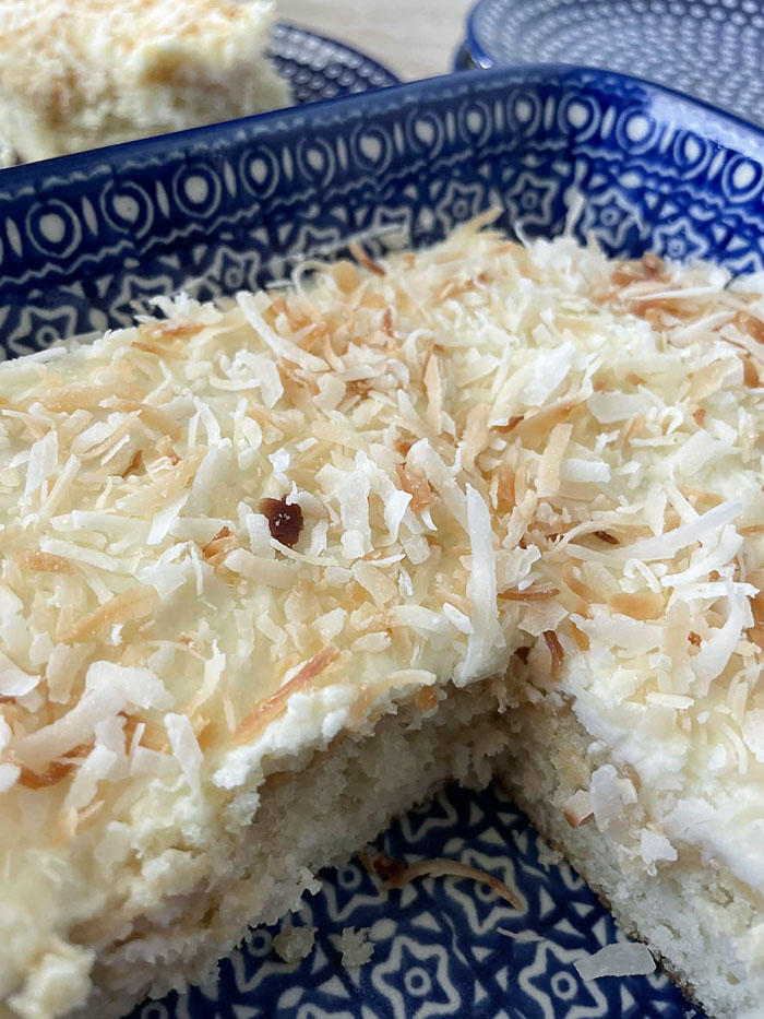 A dark blue and white pattern 9x13 Polish pottery dish of Coconut Cake with a piece cut out.