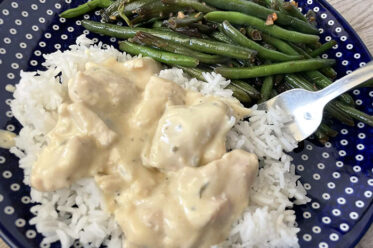 Creamy Italian chicken sauce served over white rice next to a serving of green beans on a dark blue plate with white polka dots with a fork sitting on the plate partially under the rice.