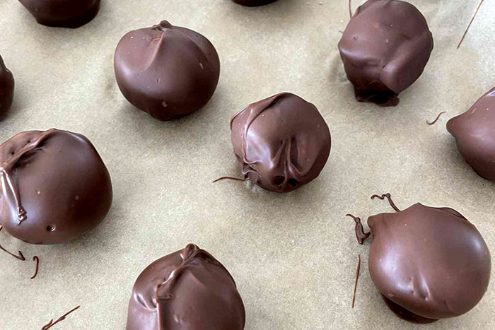 Several chocolate-covered peanut butter balls on a baking sheet lined with parchment paper.