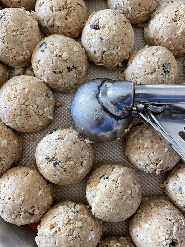 Protein Power Balls sitting on a baking mat with a small cookie scoop facing down in the middle.