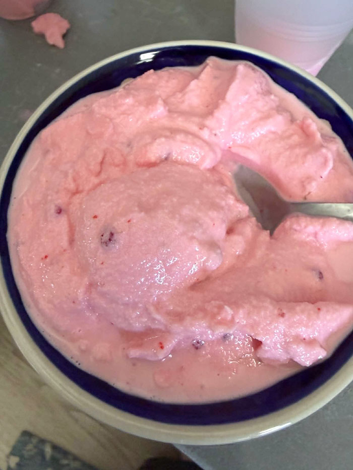 A bowl of raspberry ice cream with a milkshake-like consistency. A spoon is inserted into the ice cream from the right.