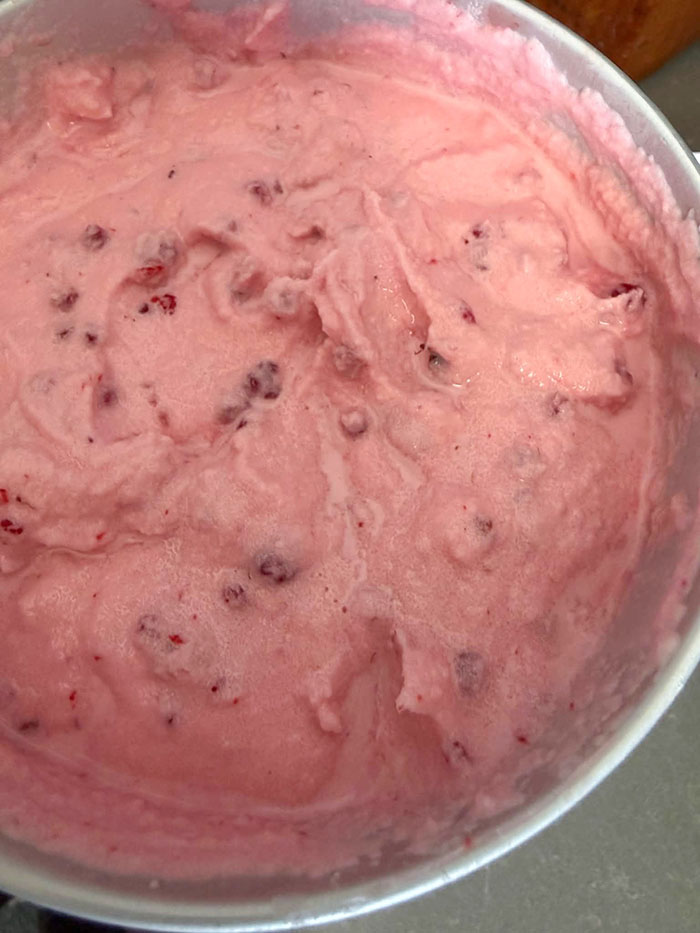 Raspberry ice cream in an ice cream maker's canister.