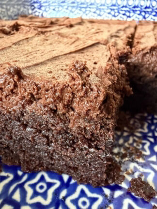 A closeup photo of a corner of a 9x13 baking dish of sliced frosted brownies with a couple of brownies missing.