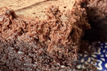 A closeup photo of a corner of a 9x13 baking dish of sliced frosted brownies with a couple of brownies missing.