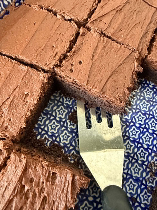 A 9x13 baking dish of cut frosted brownies with a few pieces missing and a serving spatula partway underneath a brownie in the middle.