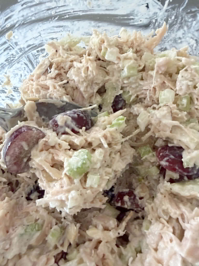 A closeup of extra protein chicken salad in a glass bowl and a spoon inserted from the left.