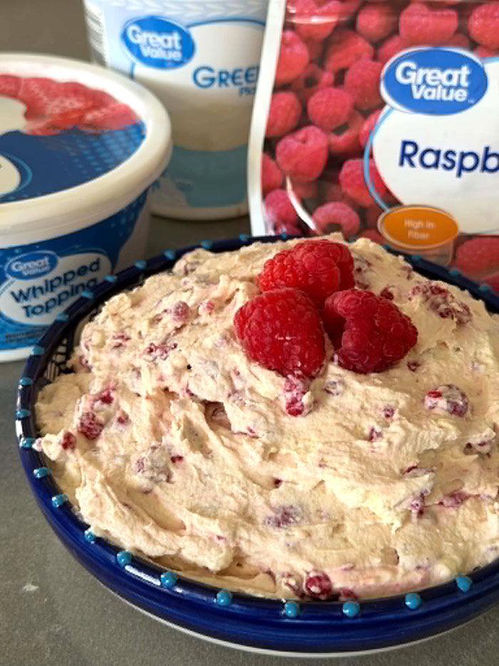 A container of whipped topping, plain greek yogurt, a bag of frozen raspberries, and a bowl of frozen berry salad topped in the middle with three whole raspberries.