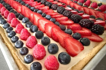 A sheet pan fruit pizza with altnerating fows of blueberries, raspberries, strawberries, and blackberries.