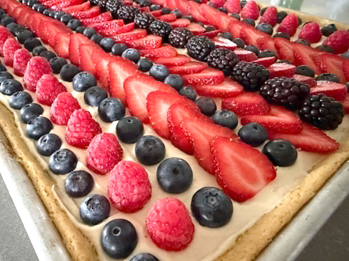 A sheet pan fruit pizza with altnerating fows of blueberries, raspberries, strawberries, and blackberries.
