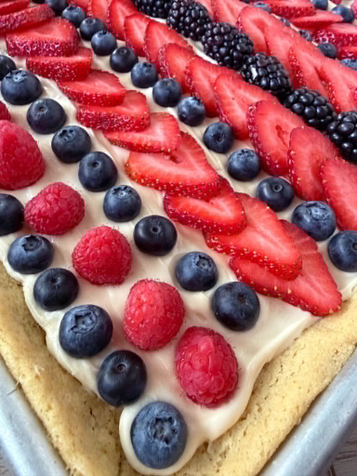 A partial picture of a sheet pan fruit pizza with rows of blueberries, raspberries, strawberries, and blackberries.