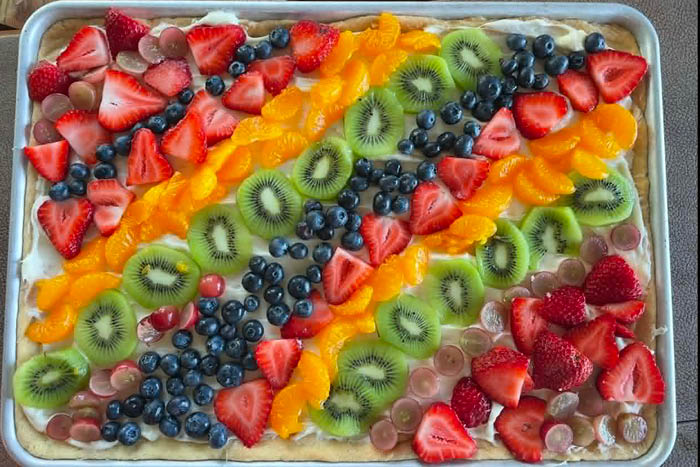 A sheet pan fruit pizza with grapes, strawberries, mandarin oranges, kiwi, and blueberries.
