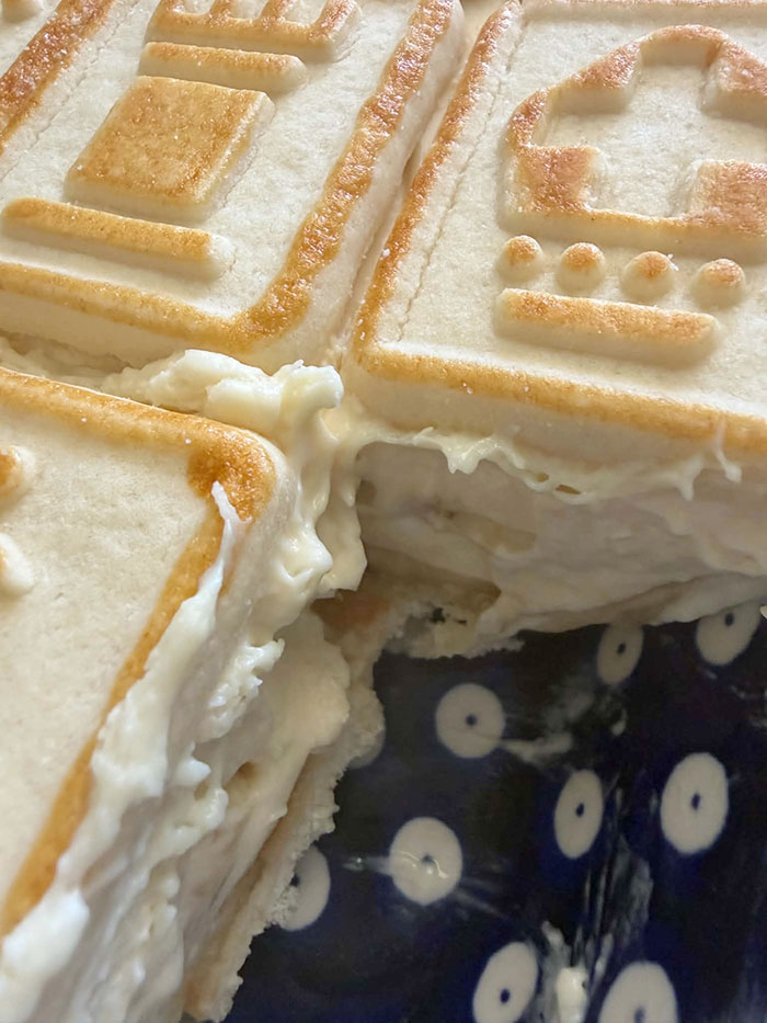 A close-up photo of a corner of a 9x13 baking dish of Banna Pudding with Chessmen Cookies with a piece cut out of the corner.