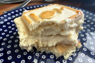 A slice of Banana Pudding with Chessmen Cookies with the corner missing from one side on a dark blue plate with white polka dots.