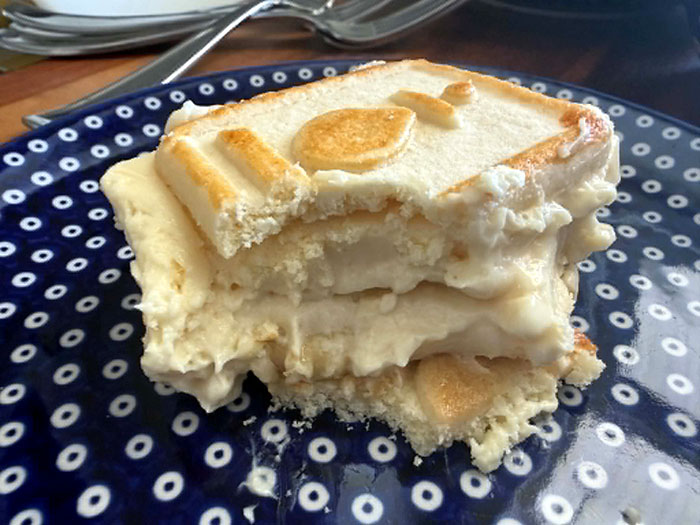 A slice of Banana Pudding with Chessmen Cookies with the corner missing from one side on a dark blue plate with white polka dots.