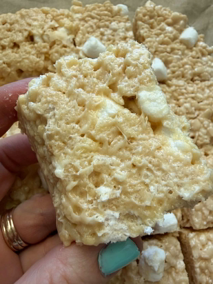 A caramel rice krispy treat held above more cut rice krispy treats.