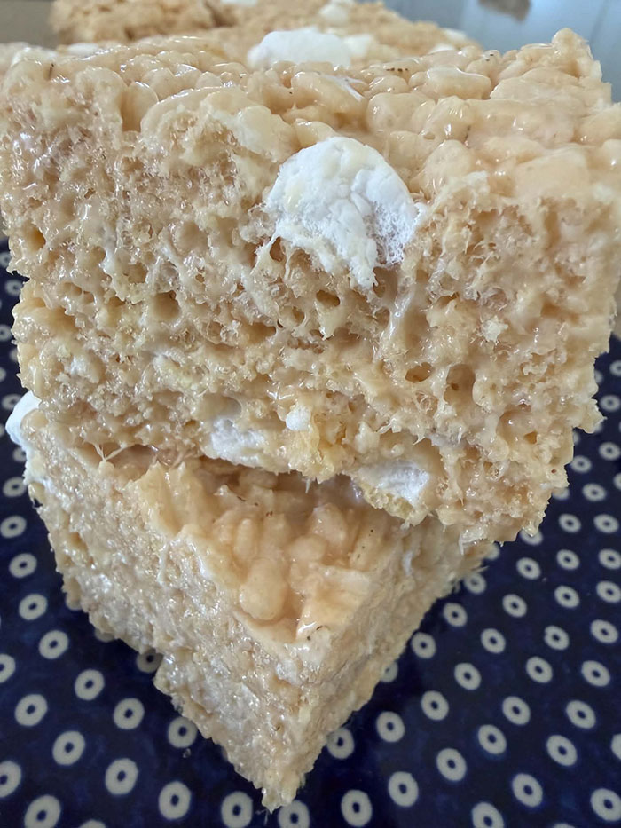 A closeup of two caramel rice crispy treats stacked on top of each other on a dark blue small plate with white polka dots.
