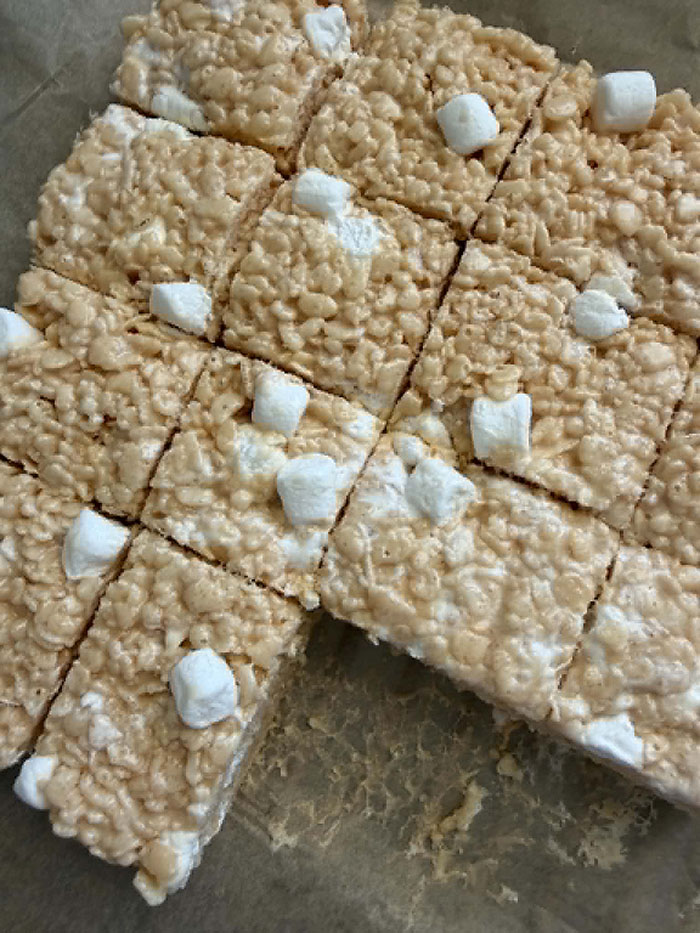 Chewy caramel rice crispy treats cut into squares sitting on brown parchment paper with two squares missing from the right corner.