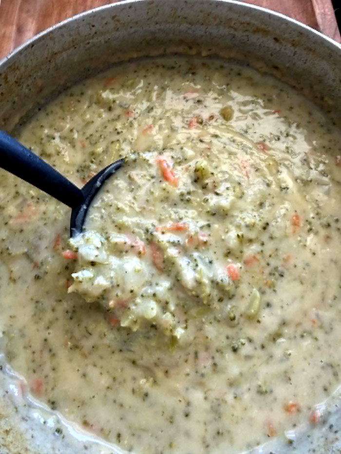 A pot of Cream of Broccoli Soup with a soup ladle held diagonally directly above from the left with soup on it.