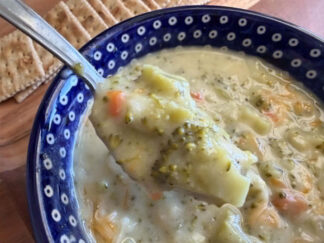 A dark blue bowl with white polka dots with Cream of Broccoli Soup. A spoon is held diagonally above from the left with soup on it.