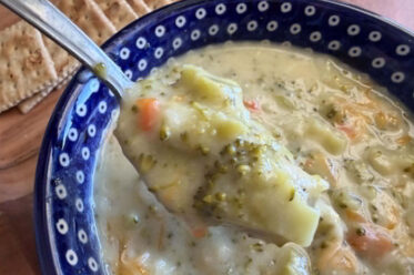A dark blue bowl with white polka dots with Cream of Broccoli Soup. A spoon is held diagonally above from the left with soup on it.