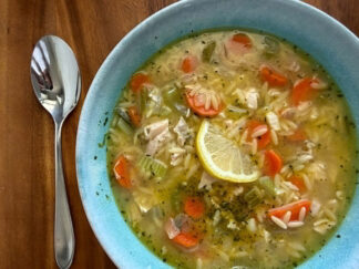 A bowl of Rotisserie Chicken Orzo Soup with a half lemon slice in the middle and a spoon on the left of the bowl.