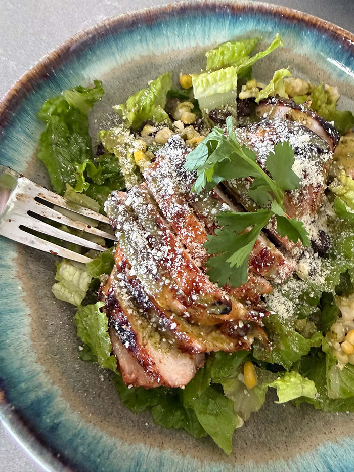 A plate of BBQ Chicken Salad with Cilantro Lime Vinaigrette with a sprig of cilantro on top and a fork-head on the left side of the plate.