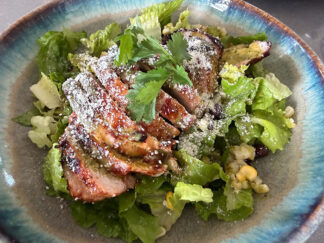 BBQ chicken salad with cilantro lime vinaigrette with a sprig of cilantro on top on a dinner plate.