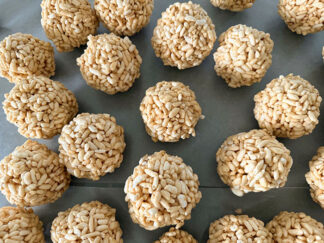 Caramel puffed rice balls sitting on a sheet of wax paper.