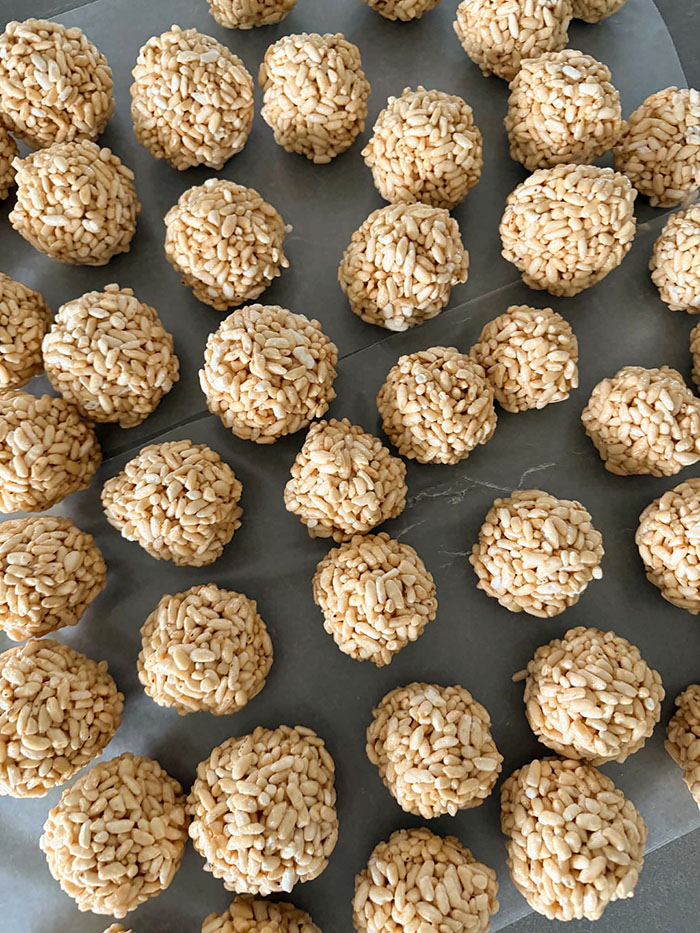 Caramel puffed rice balls sitting on two sheets of wax paper.